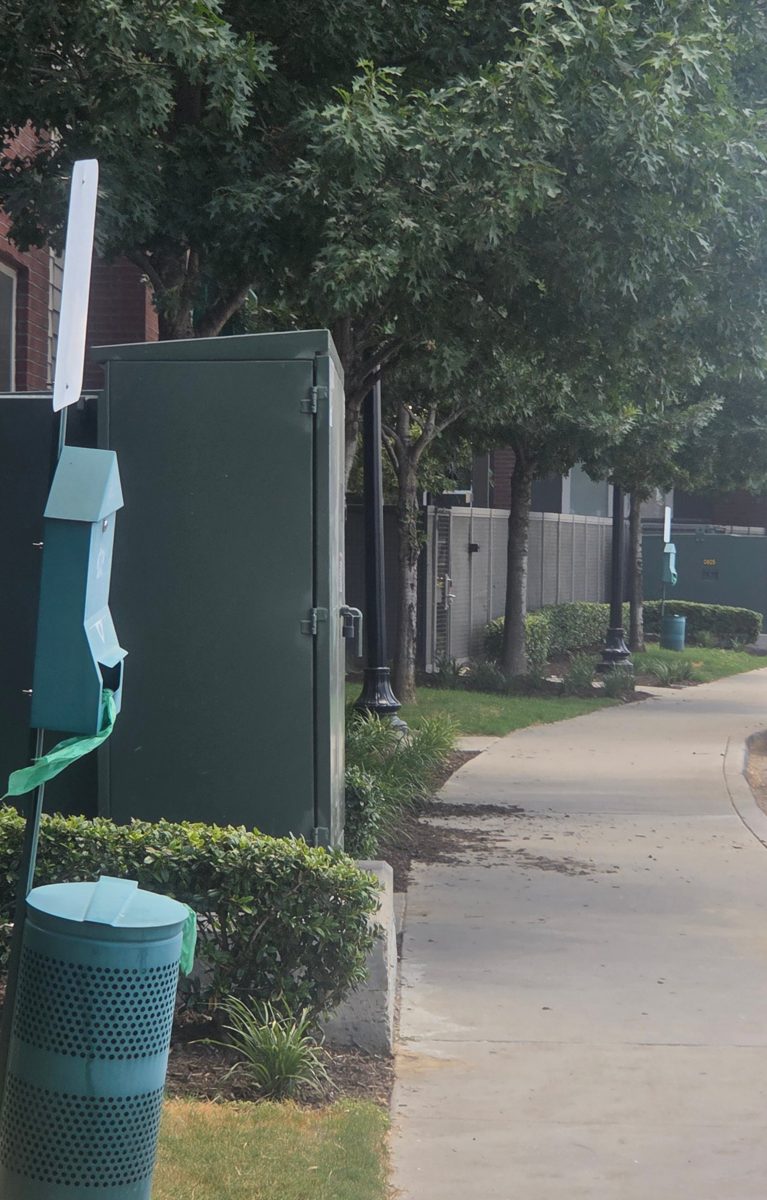 Pet waste stations with bag dispensers and bins along a tree-lined Carrollton sidewalk